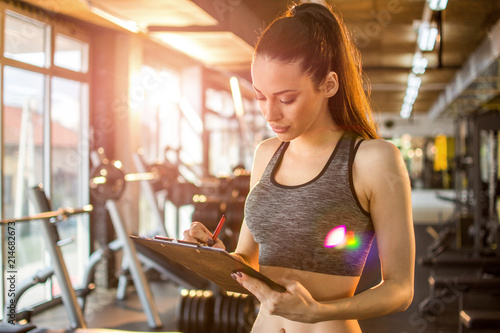 Female personal trainer or fitness instructor writing on clipboard in the gym photo