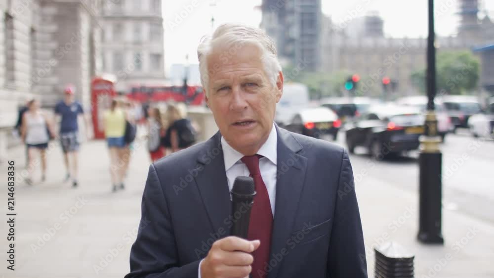 Refined mature news reporter talking into camera holding a microphone in the city