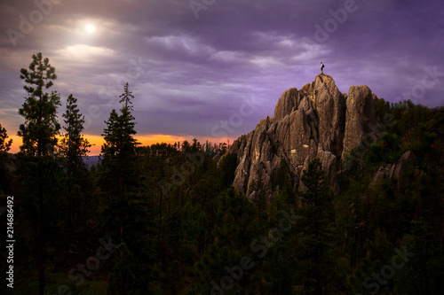 Climber standing on rocky formation in Black Hills top with a gorgeous landscape view of a forest sunset 