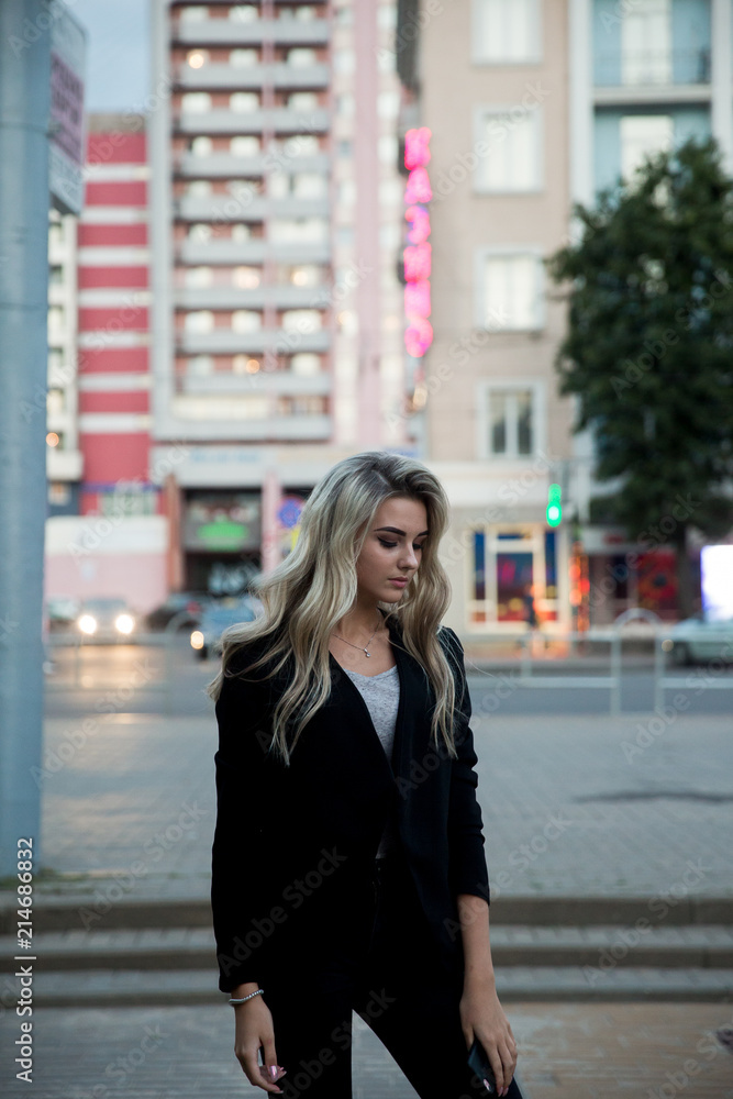Fototapeta premium Girl in black trousers and jacket.The blonde in the black suit.Blonde posing in the city