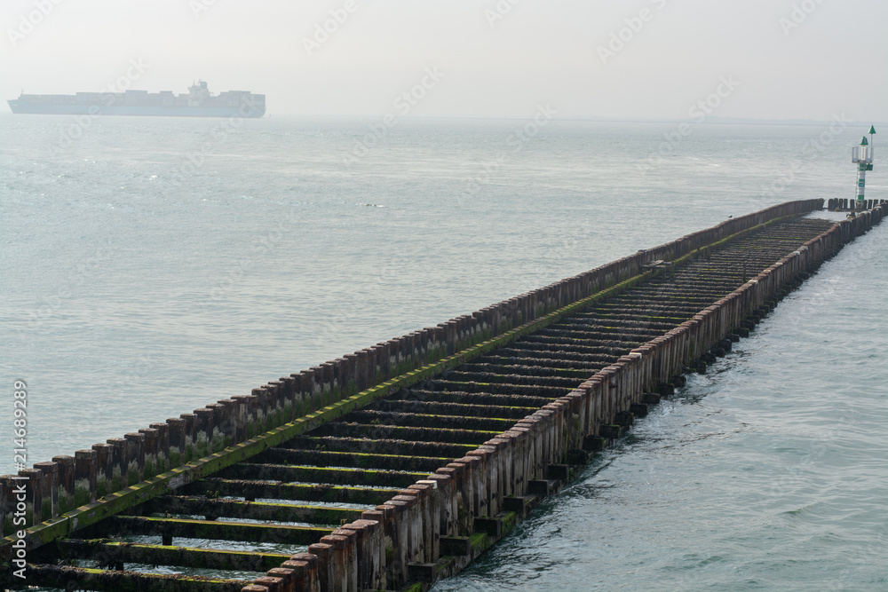 Sea near Vlissingen, Zeeland, Netherlands, old wooden pier at high tide and big cargo ship on horizon
