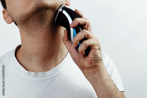 Shaving with electric shaver. Man is holding a shaver in his hand. Concept of cutting off facial hair, getting rid of beards, mustaches. Taking care of a man. Preparation for Man to leave.