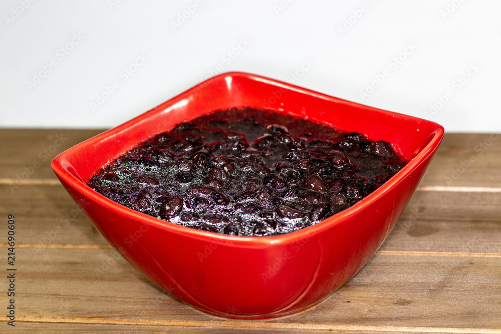 Red bowl filled with black bean soup ready to eat on the kitchen table