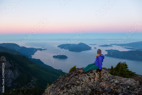 Adventurous woman on top of a mountain cliff is enjoying the beautiful summer sunrise. Taken on Mount Brunswick  Lions Bay  North of Vancouver  BC  Canada.