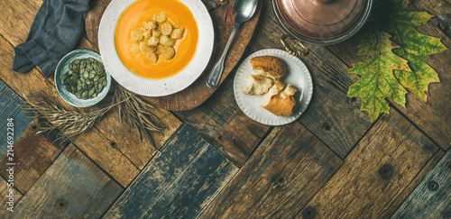 Fall warming pumpkin cream soup with croutons and seeds on board over wooden background, copy space, flat-lay, top view. Autumn vegetarian, vegan, healthy comfort food eating concept