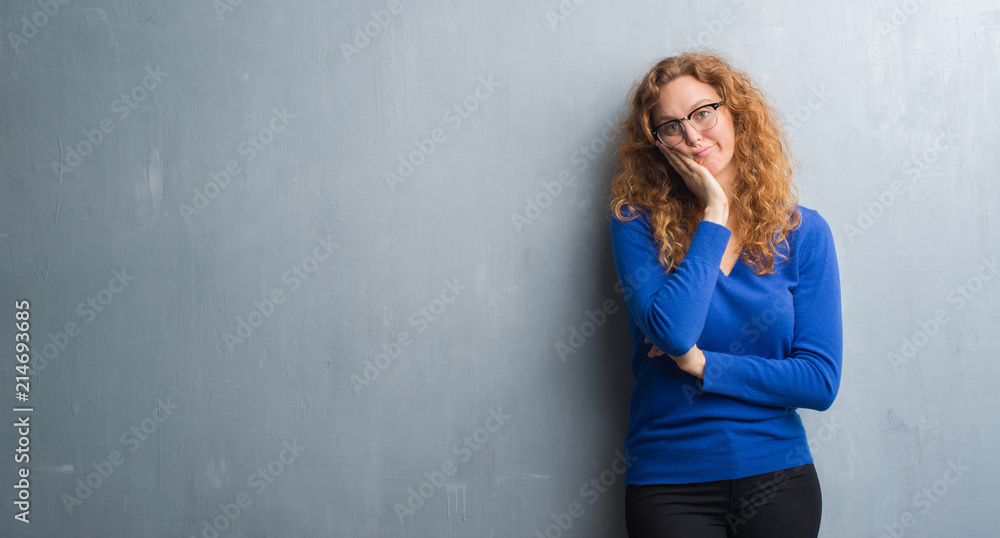 Young redhead woman over grey grunge wall thinking looking tired and bored with depression problems with crossed arms.