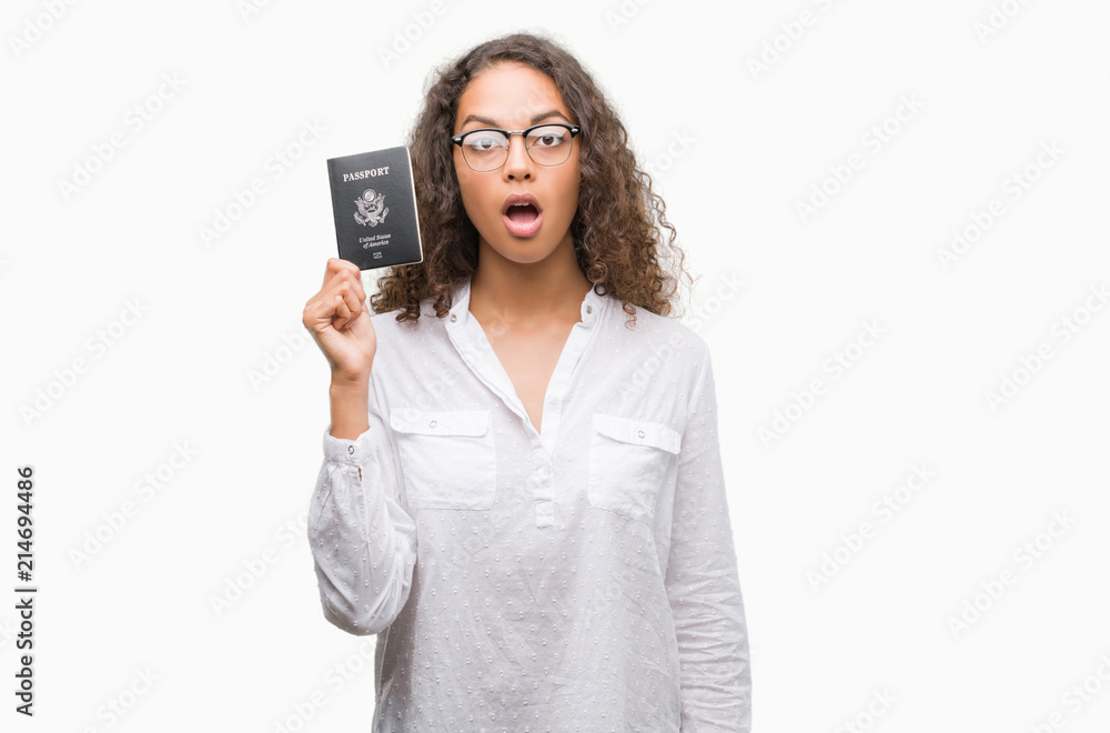 Young hispanic woman holding passport of United States of America scared in shock with a surprise face, afraid and excited with fear expression Young hispanic woman holding passport of United States of America scared in shock with a surprise face, afraid and excited with fear expression