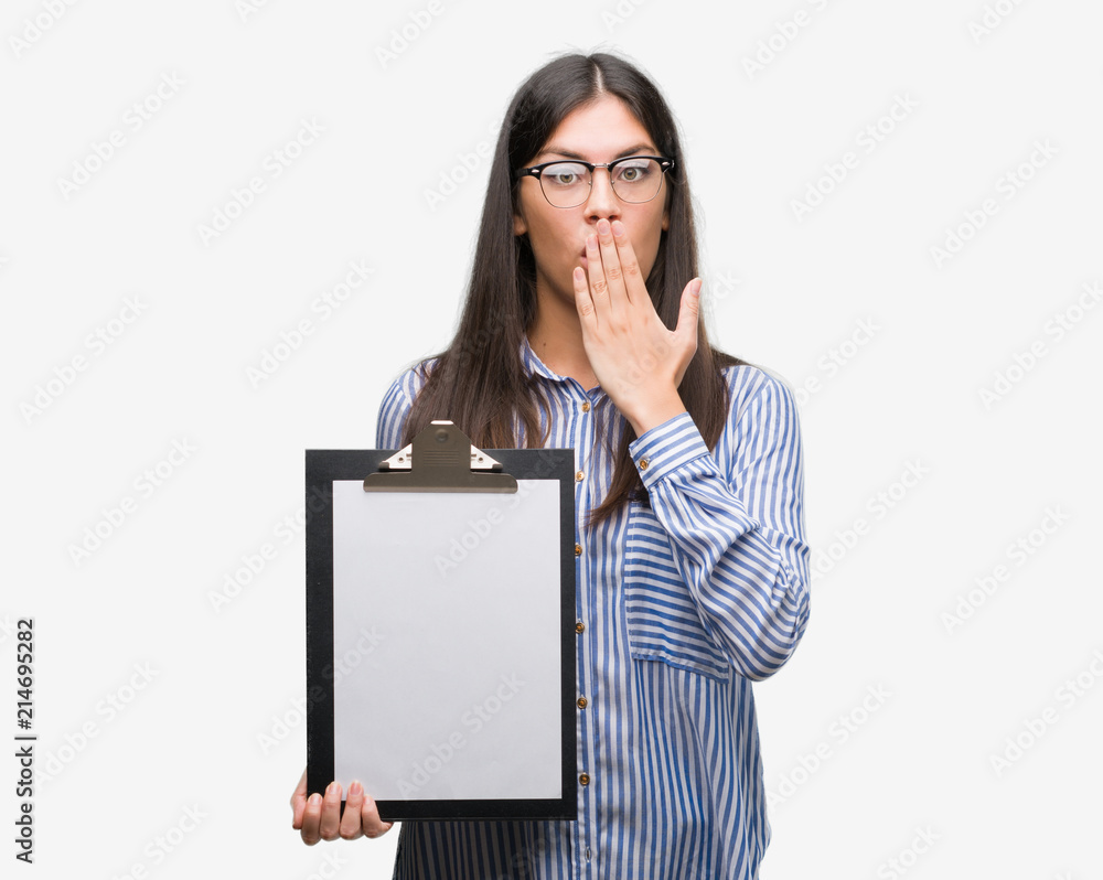 Young hispanic woman holding clipboard cover mouth with hand shocked with shame for mistake, expression of fear, scared in silence, secret concept Young hispanic woman holding clipboard cover mouth with hand shocked with shame for mistake, expression of fear, scared in silence, secret concept