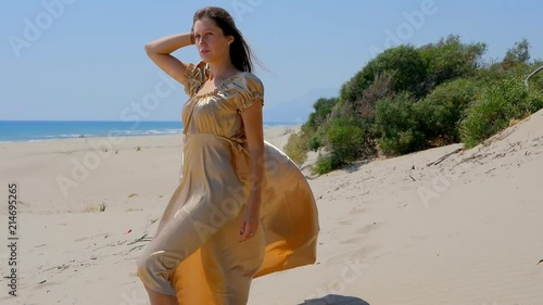 Young beautiful woman in golden long dress standing on sand dunes near the sea. photo