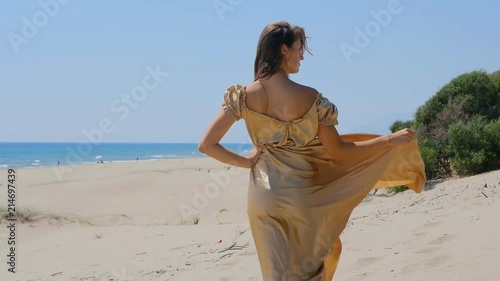 Young beautiful woman in golden long dress standing on sand dunes near the sea. photo