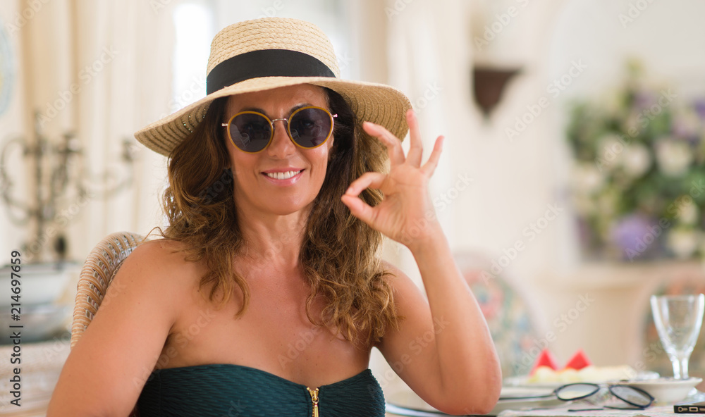 Middle age brunette woman wearing sunglasses doing ok sign with fingers, excellent symbol
