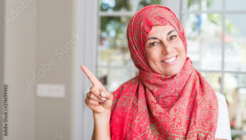Middle aged muslim woman wearing hijab very happy pointing with hand and finger to the side