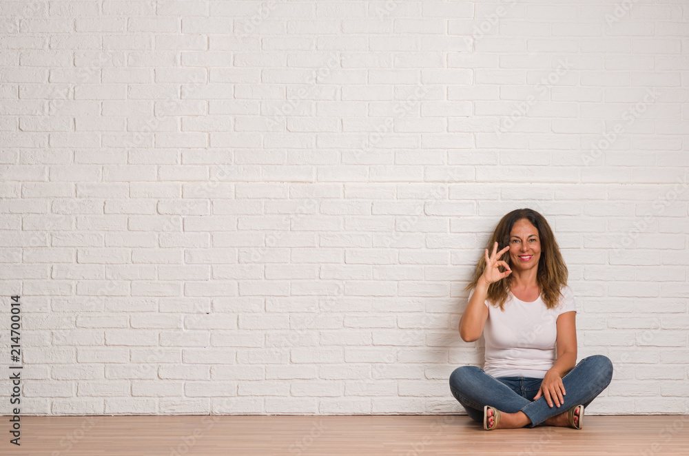 Middle age hispanic woman over white brick wall doing ok sign with fingers, excellent symbol Middle age hispanic woman over white brick wall doing ok sign with fingers, excellent symbol