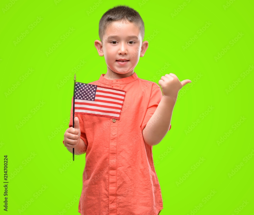 Dark haired little child holding United States flag pointing with hand and finger up with happy face smiling Dark haired little child holding United States flag pointing with hand and finger up with happy face smiling