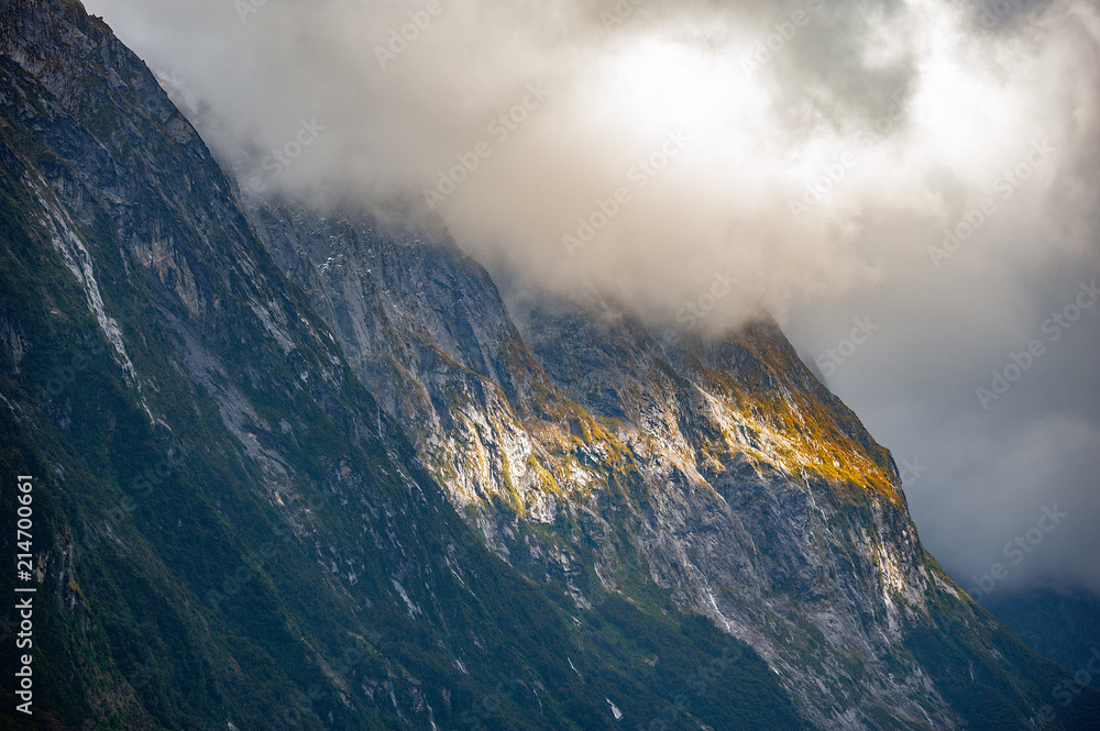 Misty and cloudy sky covering mountain top with some sunlight shining through at Milford Sounds, New Zealand.