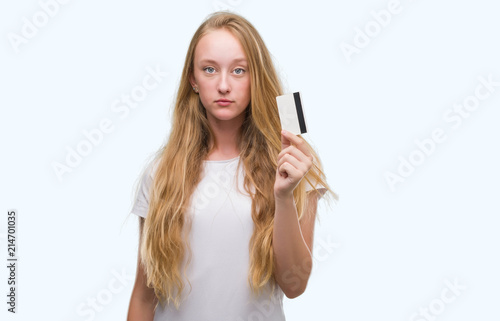 Blonde teenager woman holding credit card with a confident expression on smart face thinking serious