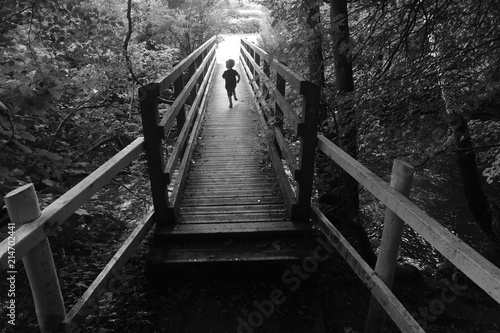 Fototapeta Naklejka Na Ścianę i Meble -  Small boy running across a bridge into the light