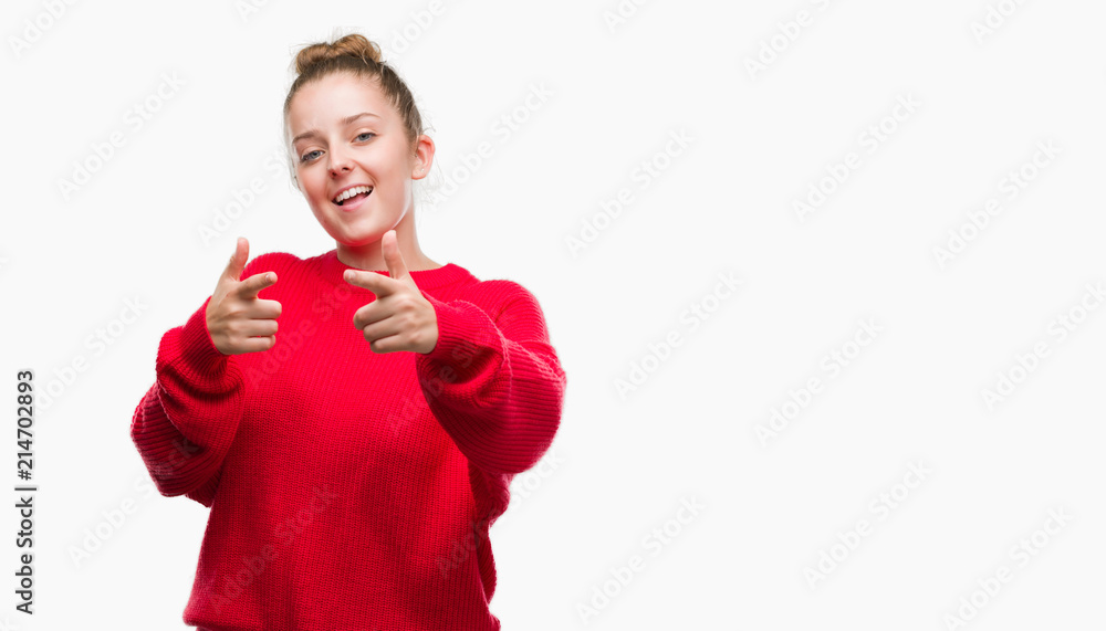 Young blonde woman wearing bun and red sweater pointing fingers to camera with happy and funny face. Good energy and vibes. Young blonde woman wearing bun and red sweater pointing fingers to camera with happy and funny face. Good energy and vibes.