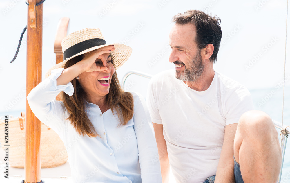 Obraz premium Middle age couple traveling on sailboat with happy face smiling doing ok sign with hand on eye looking through fingers