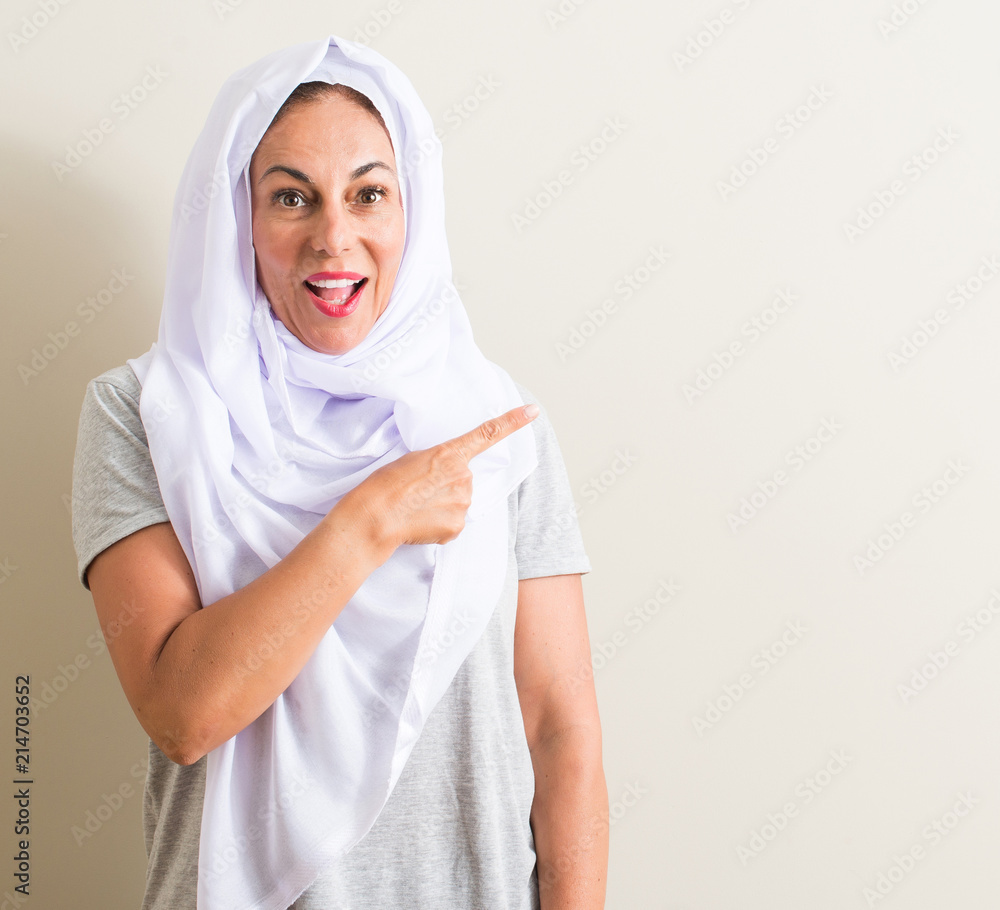 Middle age arabian woman wearing white hijab very happy pointing with hand and finger Middle age arabian woman wearing white hijab very happy pointing with hand and finger