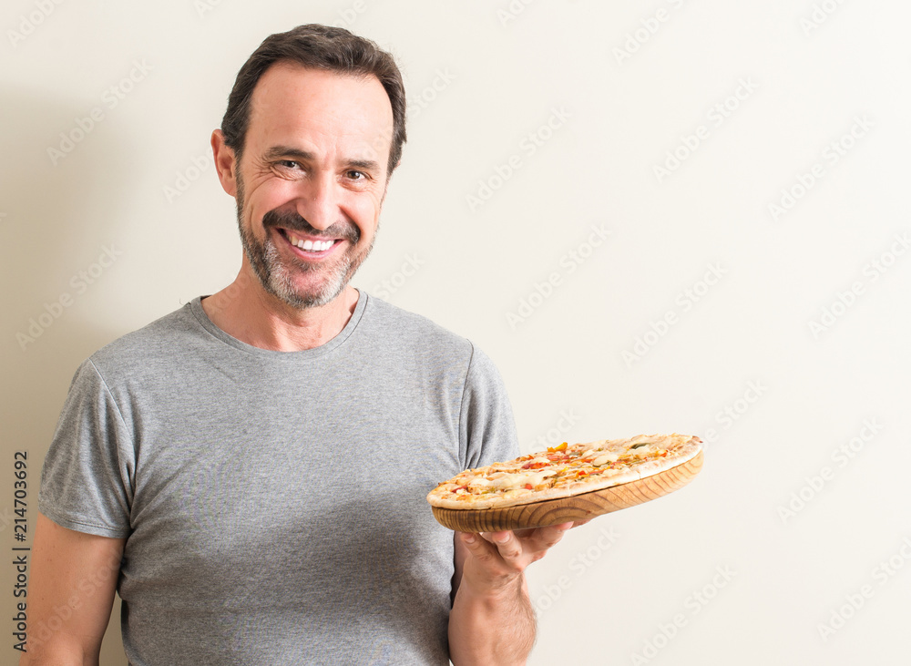 Senior man holding pizza with a happy face standing and smiling with a confident smile showing teeth Senior man holding pizza with a happy face standing and smiling with a confident smile showing teeth