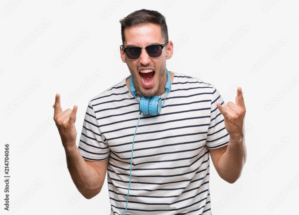 Handsome young man wearing headphones shouting with crazy expression doing rock symbol with hands up. Music star. Heavy concept. Handsome young man wearing headphones shouting with crazy expression doing rock symbol with hands up. Music star. Heavy concept.