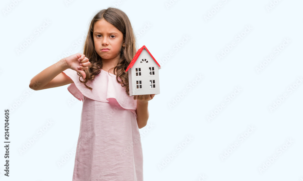 Brunette hispanic girl holding little house with angry face, negative sign showing dislike with thumbs down, rejection concept Brunette hispanic girl holding little house with angry face, negative sign showing dislike with thumbs down, rejection concept