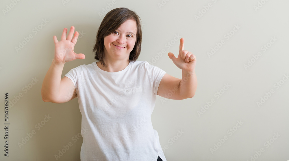 Down syndrome woman standing over wall showing and pointing up with fingers number seven while smiling confident and happy. Down syndrome woman standing over wall showing and pointing up with fingers number seven while smiling confident and happy.