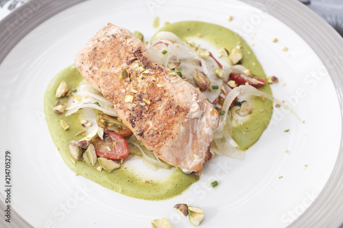 Grilled salmon steak served with green pesto sauce on top with pistachio