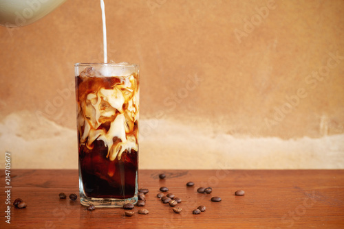 Photographie Pouring milk into a glass of homemade cold brew coffee on wooden table