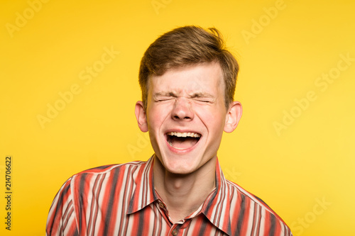 lol lmfao. man laughing hard. joy happiness humor and wide cheerful smile concept. portrait of a young guy on yellow background. emotion facial expression and feelings. photo