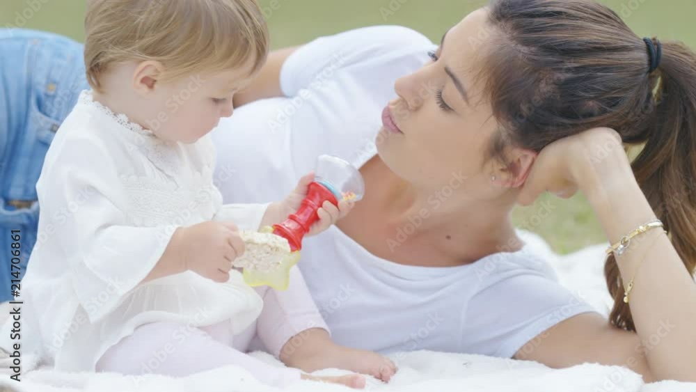 Young mother and daughter relaxing in a park and playing with baby toys Young mother and daughter relaxing in a park and playing with baby toys