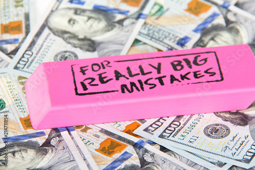 Scattered US dollars with message on pink eraser for big mistakes and savings. Concept fixing financial, business, taxes, savings, loan mistakes photo