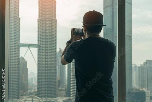 Young man traveler take a photo of cityscape of Kuala Lumpur Panorama at twilight by smartphone in hotel at Kuala Lumpur, Malaysia photo