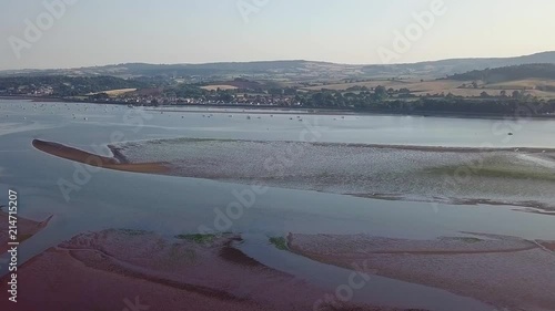 Drone flying in a clear sky towards the coastal town of Lympstone England. Agricultural lands and fields are visible. Hills and houses are in the distance. Perfect for a holiday or business trip. photo