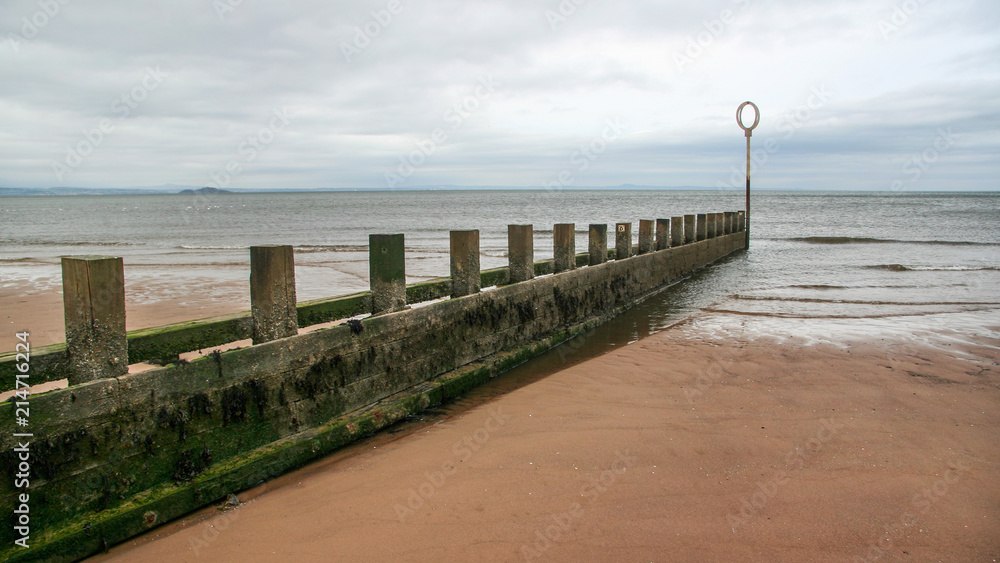 Old wooden and stone groyne structure covered with green algae on Portobello beach, low tide North sea in the backgroud, on overcast day. Edinburgh, Scotland. Old wooden and stone groyne structure covered with green algae on Portobello beach, low tide North sea in the backgroud, on overcast day. Edinburgh, Scotland.