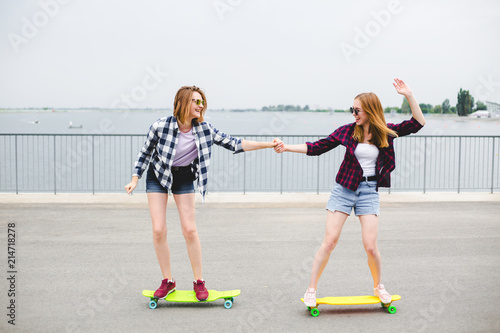 Two smiling female friends learning riding longboard with helping each other. Friendship concept