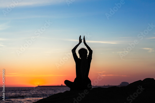 Yoga woman meditation silhouette on ocean coast during amazing sunset.