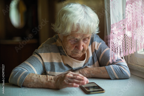 An elderly woman sits with smartphone at the table.