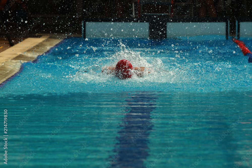 Swimmer wearing red cap practice butterfly stroke in a swimming pool for competition or race