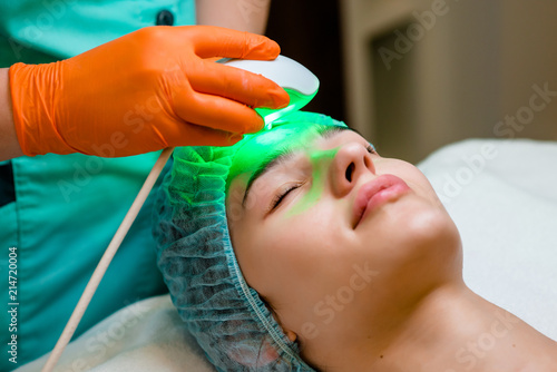 The cosmetologist makes the apparatus a procedure of Hardware face cleaning with a soft rotating brush of a beautiful, young woman in a beauty salon. Cosmetology and professional skin care. photo