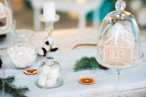 New year table setting. Gingerbread house and marshmallow in transparent glasses. Place, background