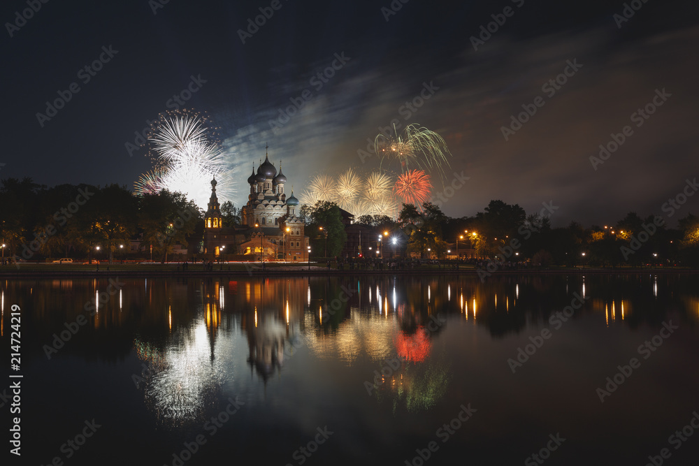 Moscow, Russia. Temple of the Holy Trinity is reflected in the pond, in the background orange, whote, green and red fireworks in honor of Victory Day (May 9)