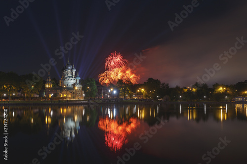 Moscow, Russia. Temple of the Holy Trinity is reflected in the pond, in the background, the blue rays of spotlights, orange and red fireworks in honor of Victory Day (May 9)