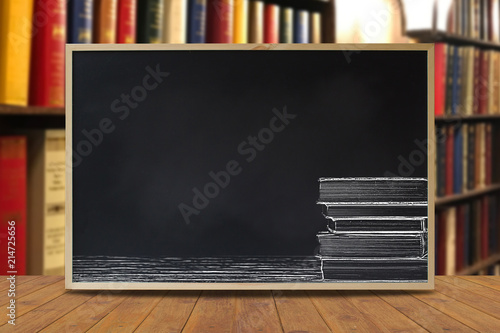 Black chalkboard with stack books chalk style on wooden table with library as background. Education concept. Empty chalkboard for advertising back to school sale. Blackboard montage for advertisement.