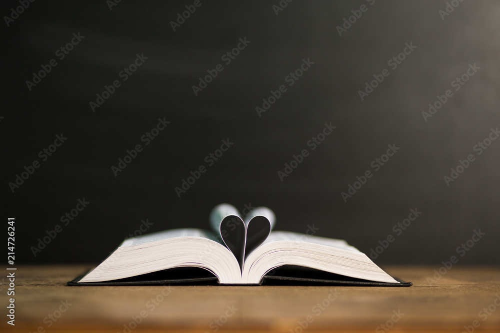 Naklejka premium Book page in heart shape with dark background. Conceptual Heart from Book. Copy Space