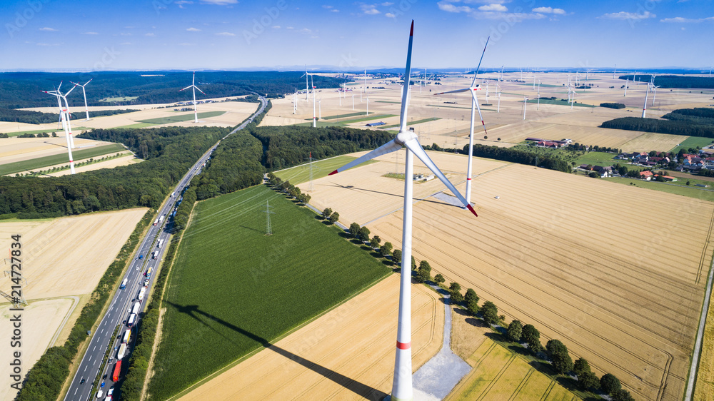 Aerial view of windmill against blue sky with clouds. Wind turbine farm and a road between agricultural fields.