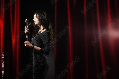 Beautiful girl in black dress singing in the microphone in the concert hall