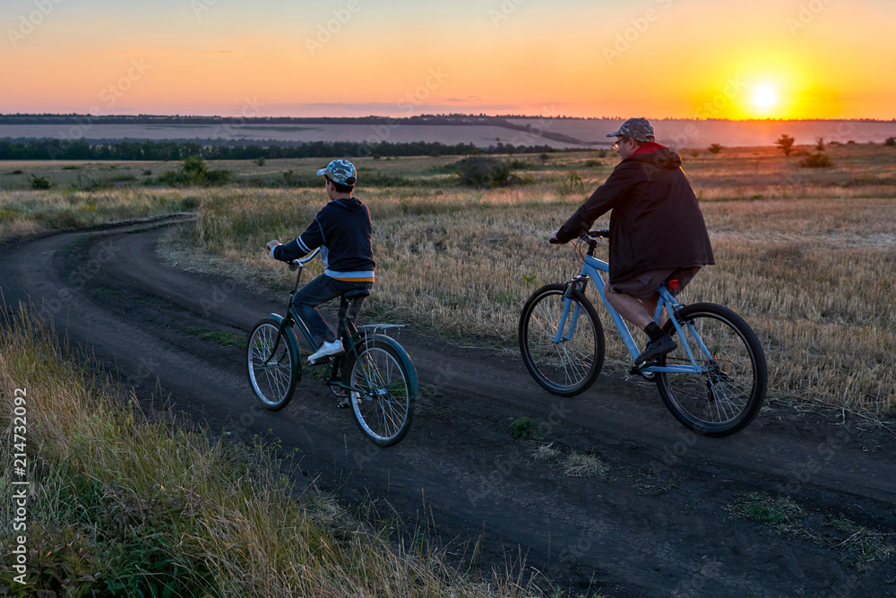 father and son ride a bike in the evening field 