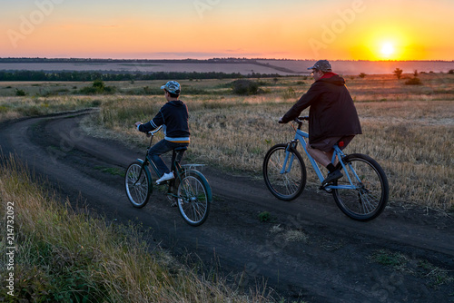 father and son ride a bike in the evening field 
